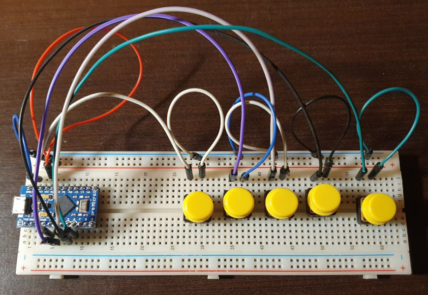 A protoboard prototype showing five push buttons arranged for one-handed operation, with basic wiring visible