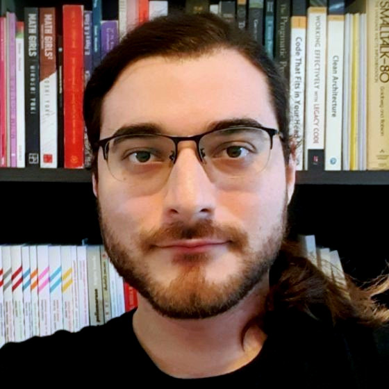 Profile photo of Facundo Javier Gelatti, which displays him in a home study, standing before a blurred bookshelf. He wears a black t-shirt and glasses, and is gazing directly ahead.